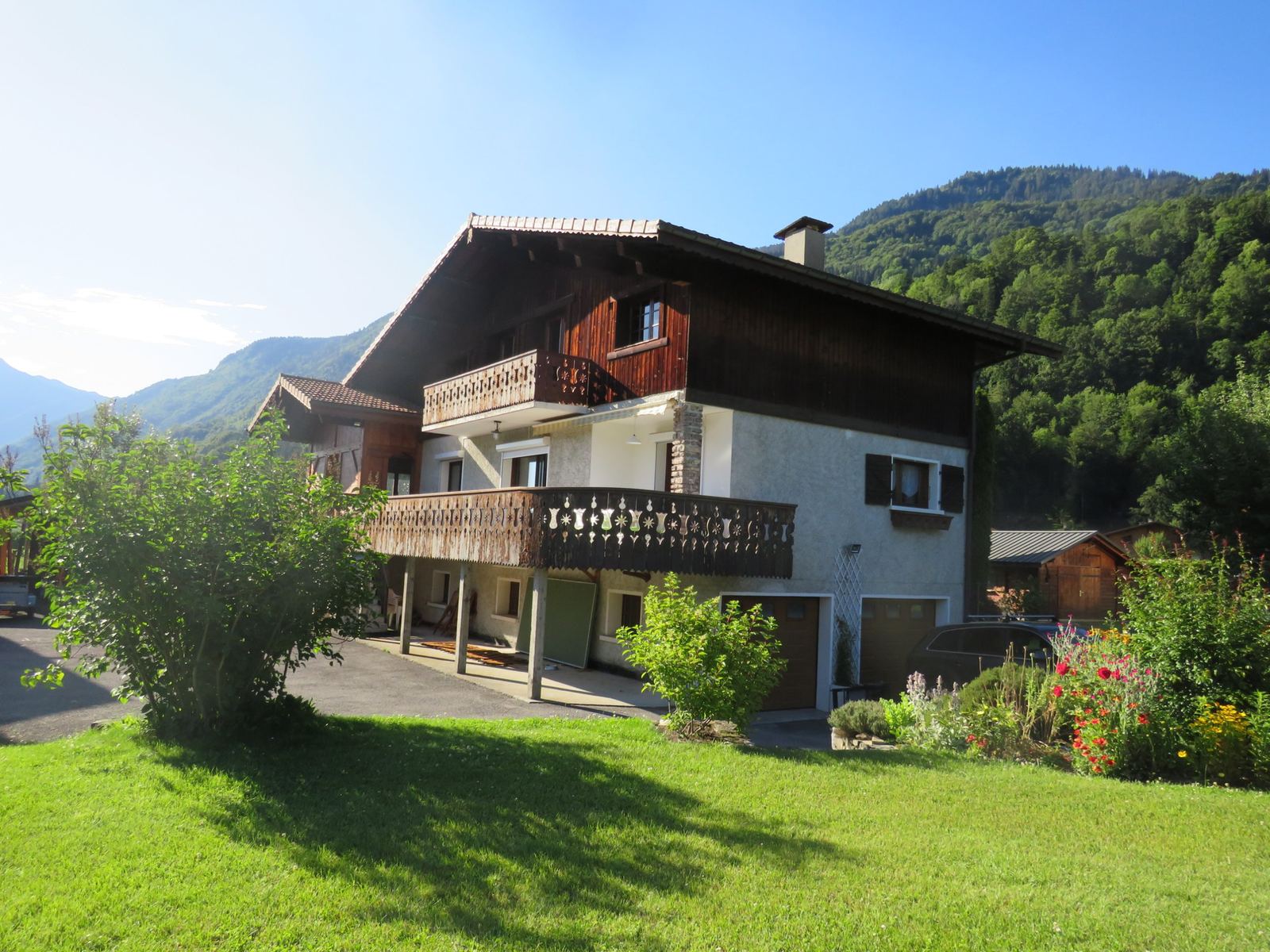Chalet Ours: a two-storey chalet with wooden balconies, a lawn and wooded mountains behind